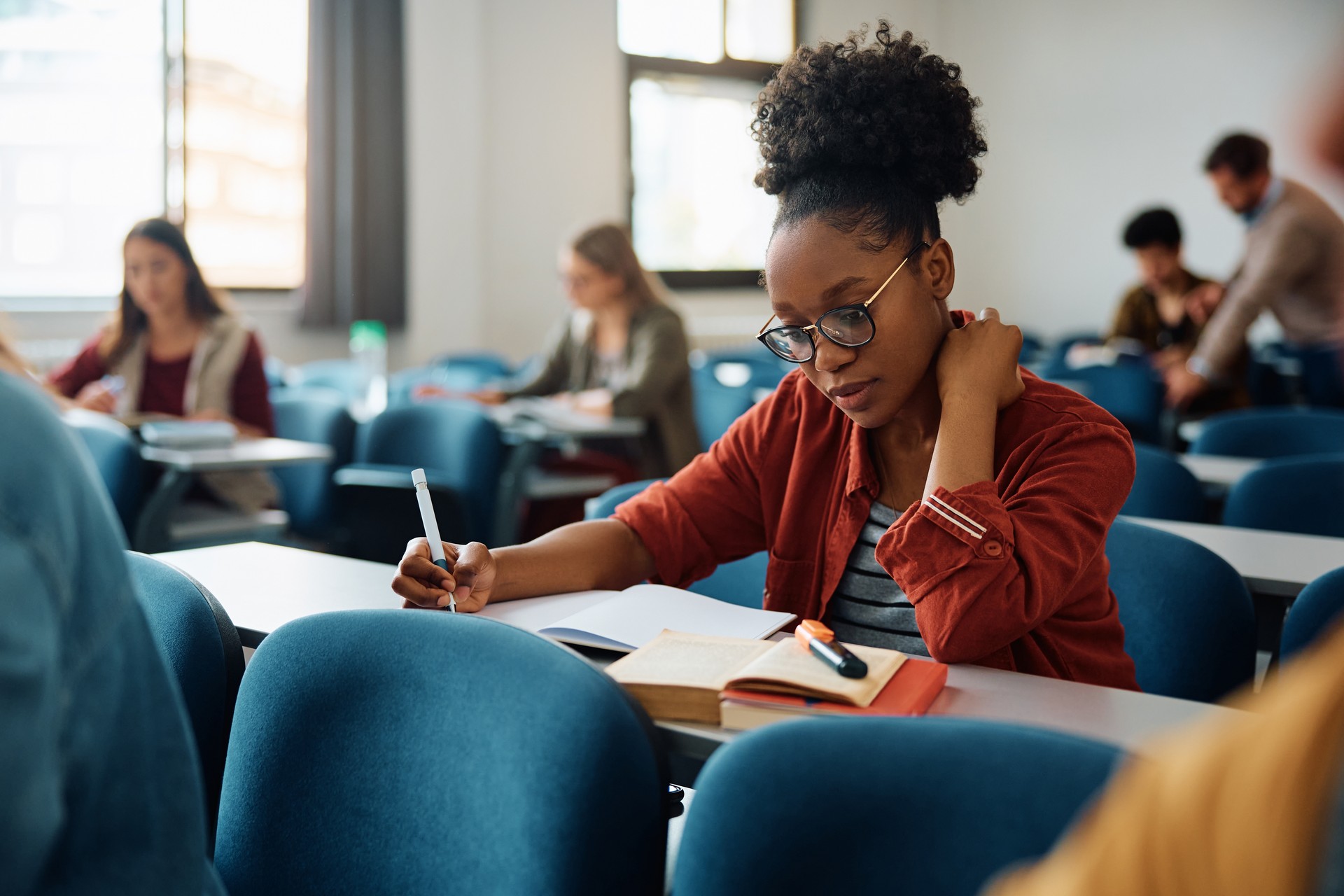 African American university student writing in her notebook while studying in the classroom.