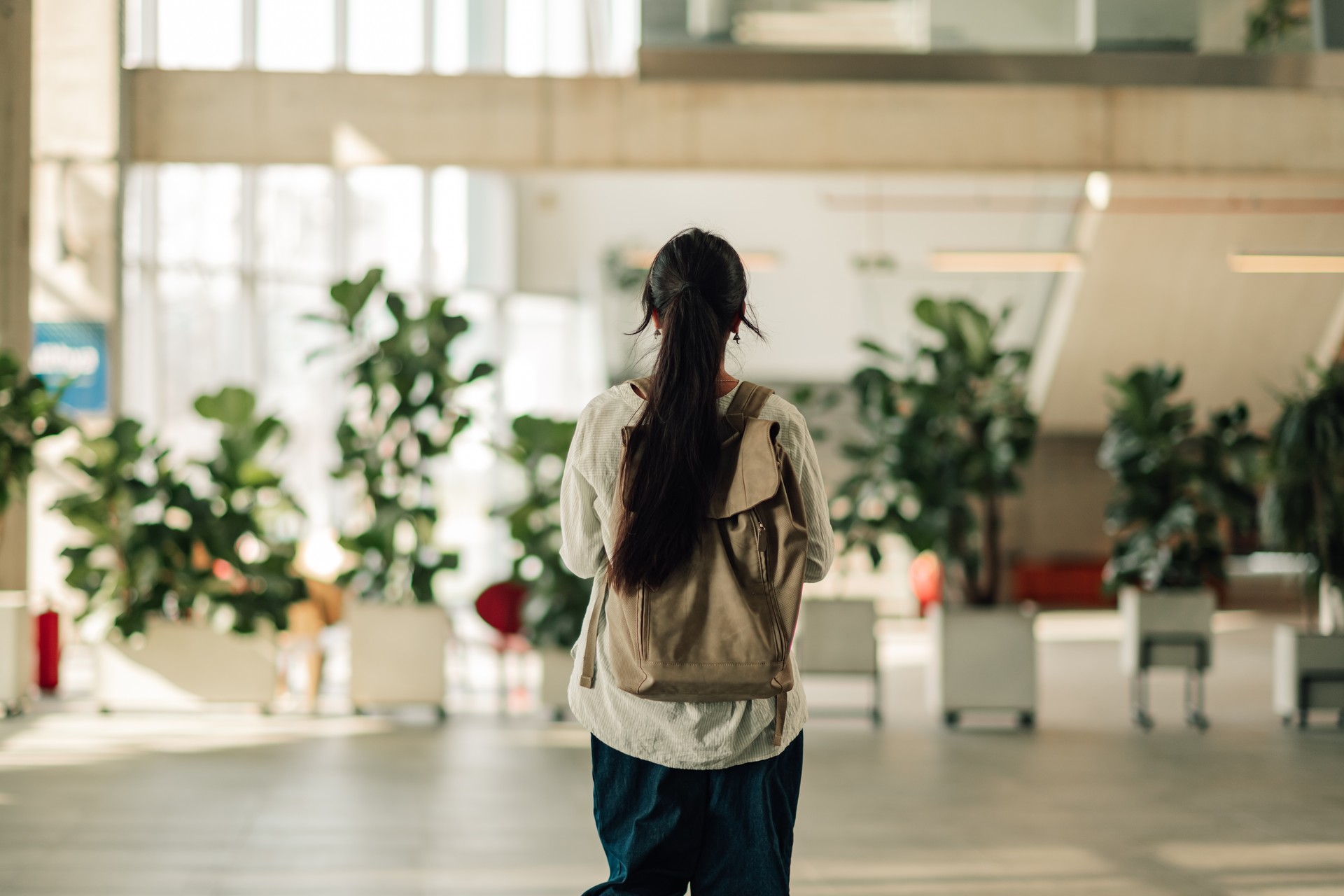 Young woman student walking through a modern university or college building, carrying a backpack, representing education and new beginnings