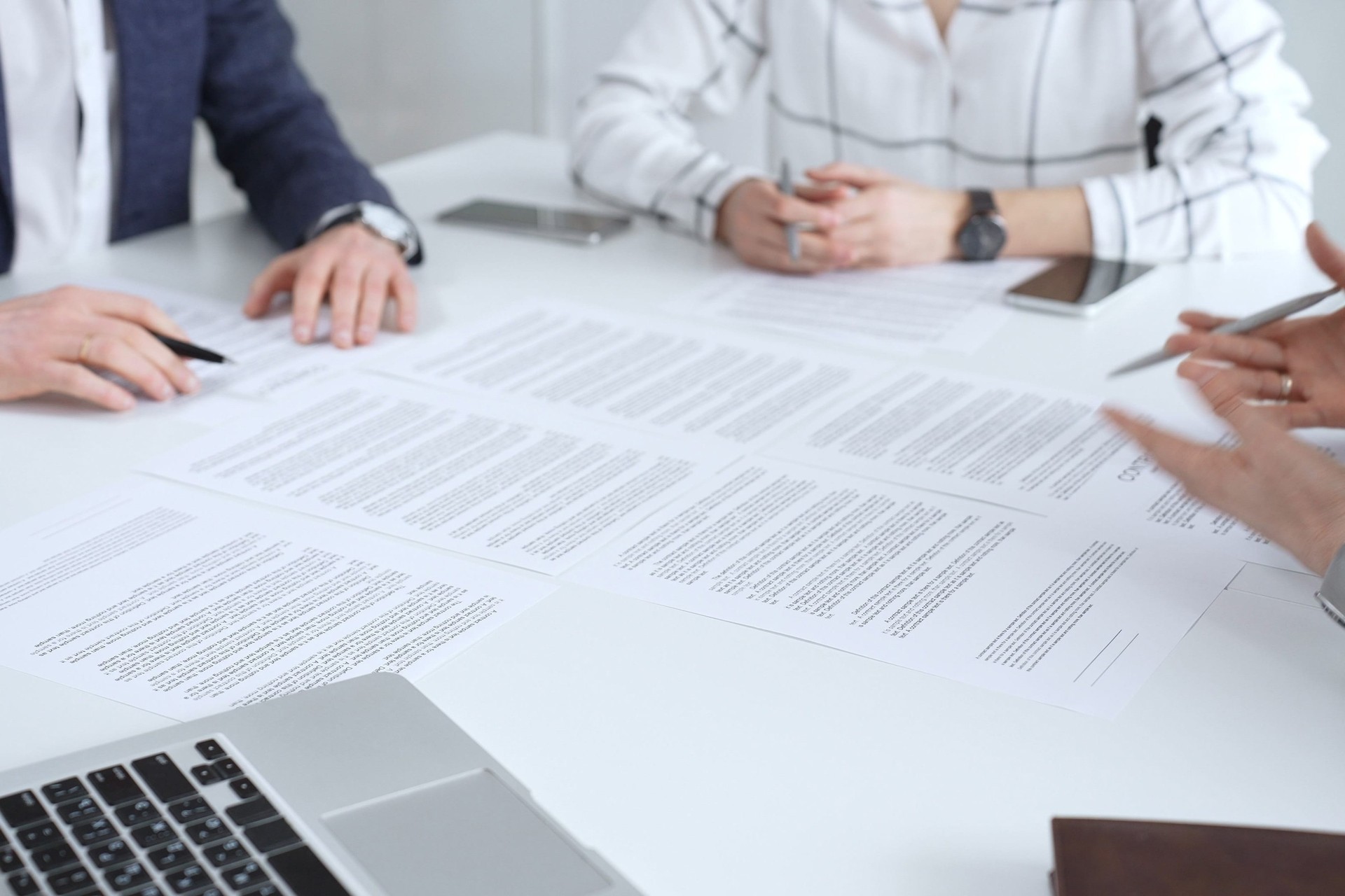 Professionals reviewing and signing contract documents across a white table, hands exchanging papers and pens to finalize negotiation, partnership and corporate agreement decisions