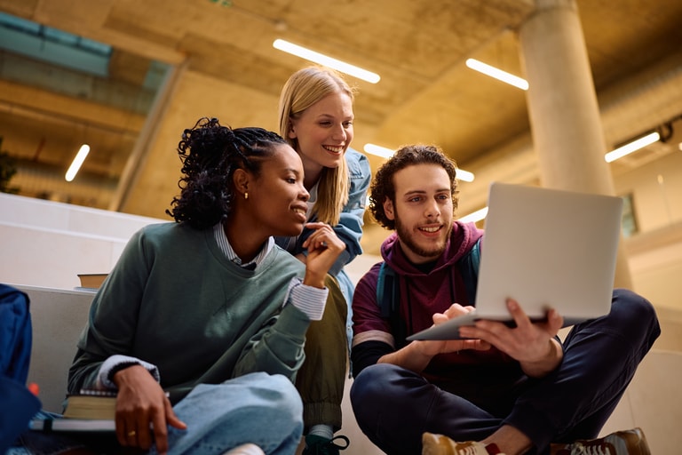 Multiracial group of happy students using laptop at the university.