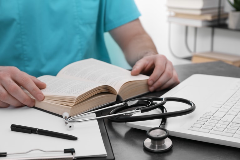 Medical student in uniform studying at table indoors, closeup
