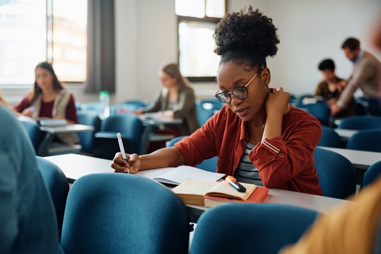 African American university student writing in her notebook while studying in the classroom.