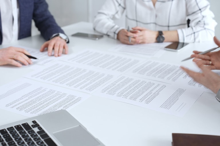 Professionals reviewing and signing contract documents across a white table, hands exchanging papers and pens to finalize negotiation, partnership and corporate agreement decisions